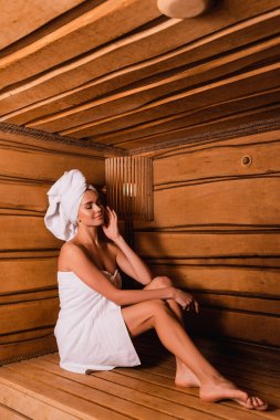 Pleased woman with closed eyes relaxing in wooden sauna  clipart