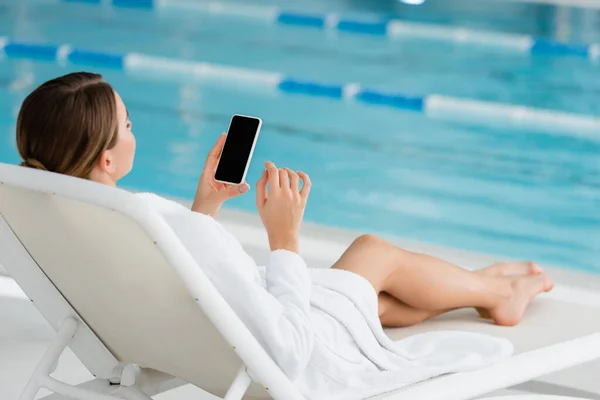 young woman resting on deck chair and using smartphone with blank screen in spa center