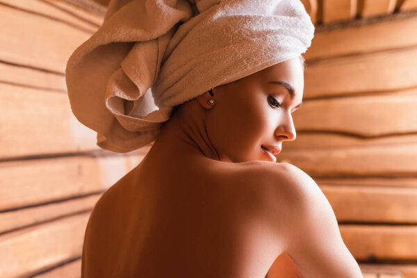 shirtless woman with towel on head relaxing in sauna 