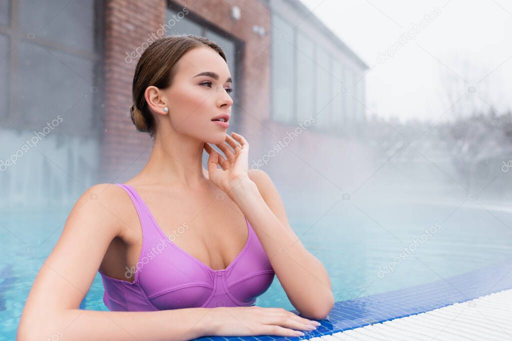 young woman with big bust looking away while bathing in outdoor swimming pool