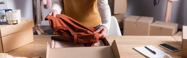 partial view of showroom owner holding sweater near carton box, banner