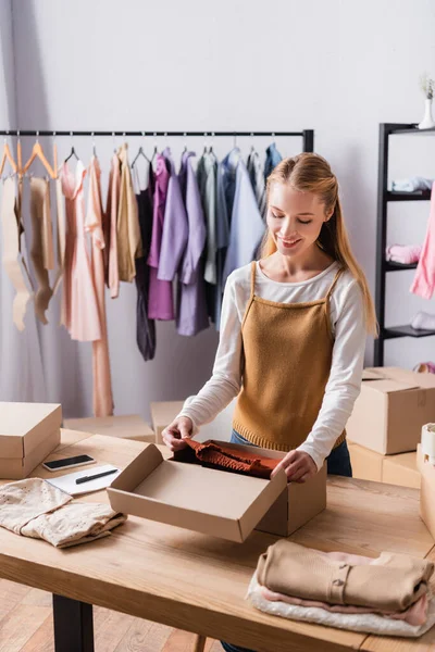 Venditore Sorridente Imballaggio Vestiti Scatole Showroom Vicino Appendini Sfondo Sfocato — Foto Stock