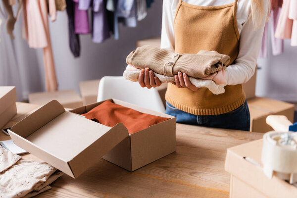 cropped view of showroom owner holding clothes near carton boxes in showroom