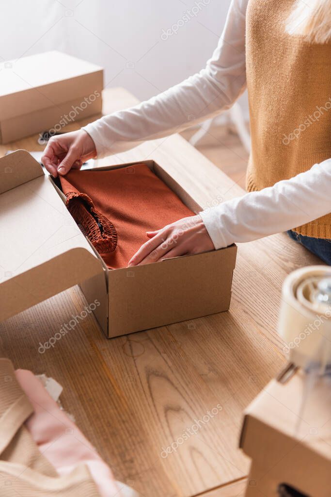 partial view of showroom proprietor packing sweater into box, blurred foreground