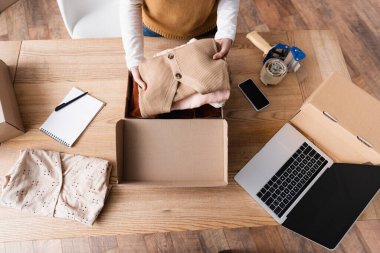 Galeri sahibinin iş yerinde karton kutuların ve aletlerin yanında giysileri tutarken kısmi görüntüsü