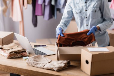 Lastik eldivenli satıcının moda mağazasında giysi paketleme görüntüsü.