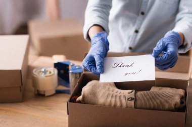 Lateks eldivenli butik satıcısının kısmi görüntüsü. Üzerinde harfler ve bulanık bir geçmiş var.