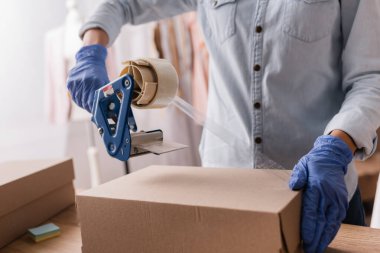Plastik eldivenli, yapışkan bantlı, arka planda bulanıklık olan kıyafet dükkanının kısmi görüntüsü