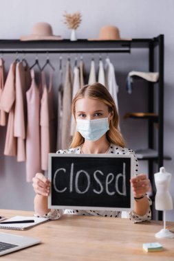 showroom owner sitting at workplace in medical mask and holding board with closed lettering clipart