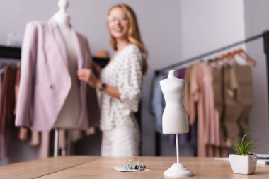 Kağıt raptiyelerinin seçici odağı, manken modeli ve sergi salonunun yakınındaki bulanık arkaplanda saksı bitkisi.