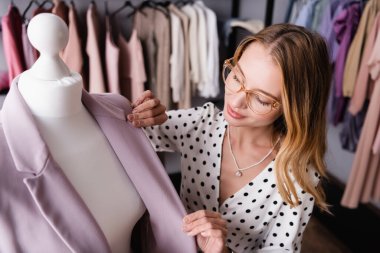 young successful businesswoman touching blazer on mannequin in showroom clipart