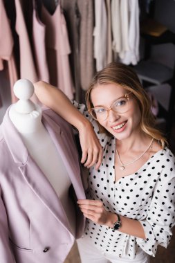 high angle view of trendy, stylish showroom owner smiling at camera near mannequin clipart