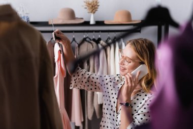 Başarılı bir galeri sahibi, bulanık ön planda asılı dururken akıllı telefondan konuşuyor