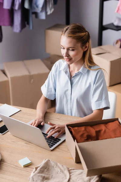 Showroom Proprietor Typing Laptop Clothes Boxes Blurred Foreground — Stock Photo, Image