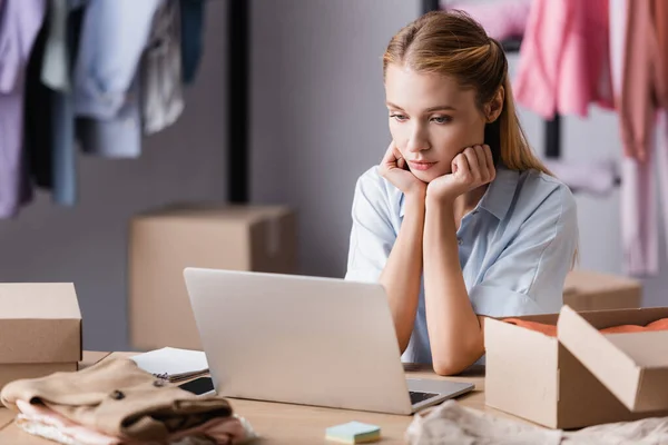 Thoughtful Businesswoman Working Laptop Carton Boxes Clothes Boutique Blurred Foreground — Stock Photo, Image
