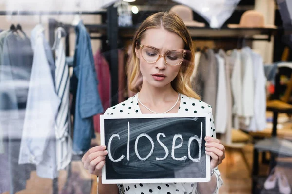 sad proprietor holding board with closed lettering in showroom