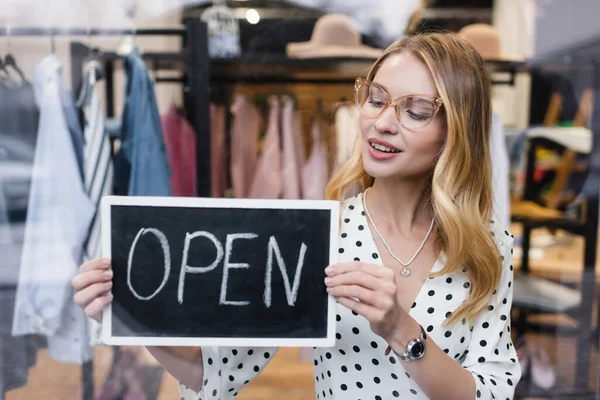 smiling proprietor holding board with open lettering in fashion boutique