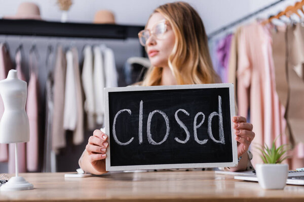 businesswoman holding board with closed lettering in showroom, blurred foreground