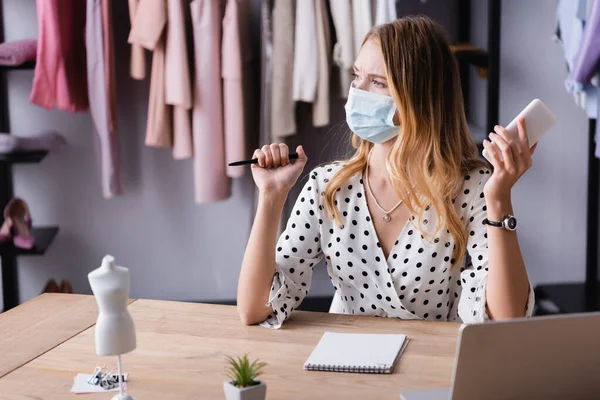 Thoughtful Proprietor Medical Mask Holding Smartphone Pen While Working Showroom — Stock Photo, Image