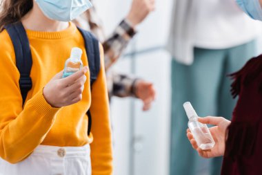 Koruyucu maskeli çocukların okulda el dezenfektanlarıyla el dezenfektanı tutmaları. 