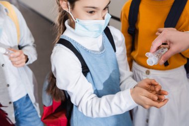 Tıp maskeli kız dezenfektan ve sınıf arkadaşlarıyla öğretmeninin yanında duruyor. 