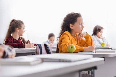 Not defterinin, kitabın ve elmanın yanında elinde kalem tutan okul çocuğu. 