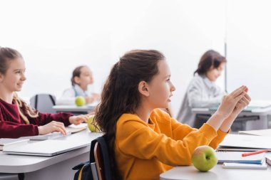 Öğrenci elma, aygıt ve not defterinin yanında oturuyor. 