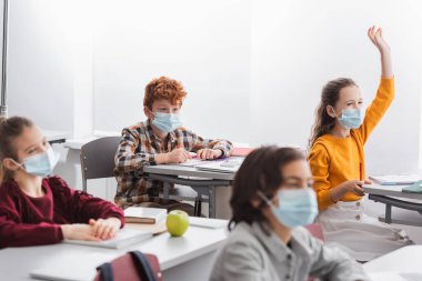 Tıp maskeli çocuklar ders sırasında sınıftaki masalarda oturuyorlar. 