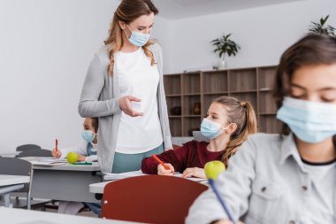 Tıp maskeli öğretmen ders sırasında kızı parmağıyla işaret ediyor.