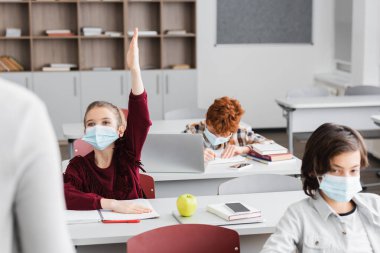 Tıp maskeli kız. Sınıf arkadaşlarının ve öğretmeninin önünde el kaldırıyor.