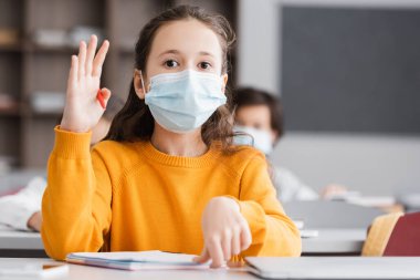 Tıp maskeli okul çocuğu ders sırasında el kaldırıyor.