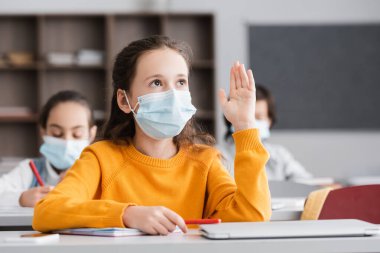 schoolgirl in medical mask raising hand during lesson clipart