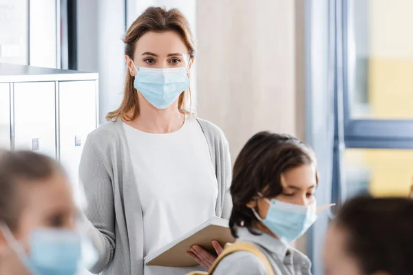 Teacher Protective Mask Holding Notebook Pupils Blurred Foreground — Stock Photo, Image