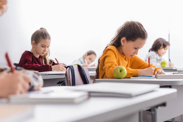 Schülerin Schreibt Neben Apfel Und Buch Auf Schreibtisch Klassenzimmer — Stockfoto