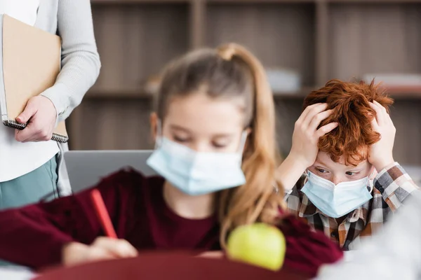 Selektywne Skupienie Zmęczonego Chłopca Masce Medycznej Dotykającego Głowy Podczas Lekcji — Zdjęcie stockowe