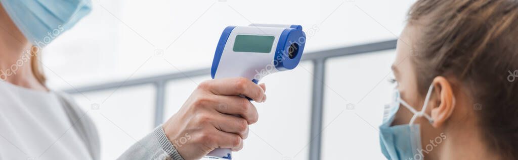 Teacher measuring temperature of pupil with non contact thermometer on blurred foreground, banner 