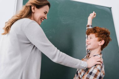 excited schoolboy showing win gesture near chalkboard and happy teacher clipart