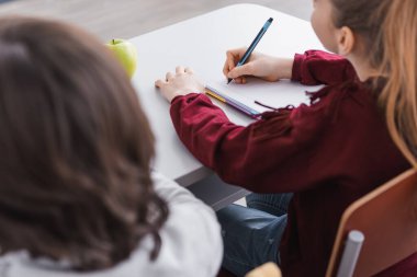 Sınıf arkadaşının yakınındaki bulanık ön planda not defterine yazan kız.