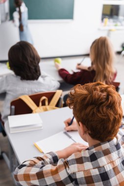 Sınıfta not defterlerine yazan öğrencilerin arka planı, bulanık arkaplan
