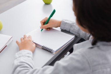 Okulda ders sırasında kalemle yazı yazan okul çocuğu, ön planda bulanıklık