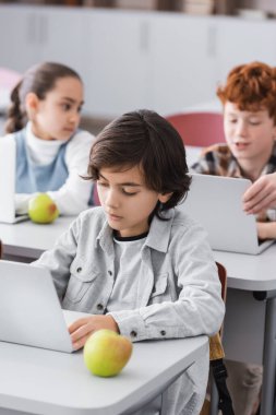 Sınıfta laptopun ve elmanın yanında konsantre okul çocuğu