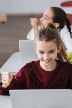 Sınıfta dizüstü bilgisayarın yanında zafer jesti gösteren heyecanlı kız.