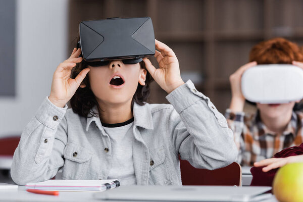 shocked schoolkid touching vr headset while gaming in school on blurred background