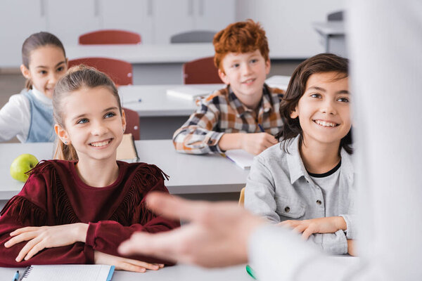 happy schoolkids listening teacher in classroom on blurred foreground