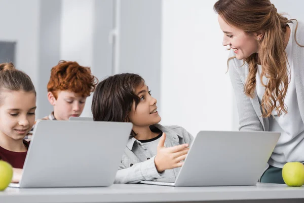 Iskolás Fiú Mutatva Laptop Közel Mosolygós Tanár Osztályteremben — Stock Fotó