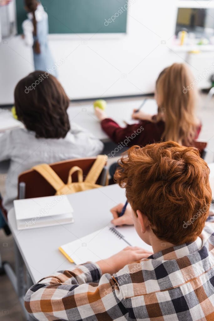 back view of pupils writing in notebooks in classroom, blurred background