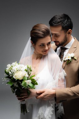 Müslüman damat, gülen geline sarıldı. Gri renkte bir düğün buketiyle. 
