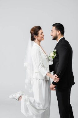 Gri renkte birbirine gülümseyen gelin ve damadın yan görünüşü 