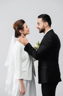 Müslüman damadın gri üzerine izole edilmiş gülen gelinin boynuna dokunuşunun yan görüntüsü 