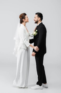 Beyaz arka planda birbirine gülümseyen çok ırklı yeni evlilerin yan görünüşü